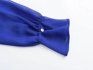 Close-up of royal blue blouse cuff with fine white button on semi-sheer chiffon fabric