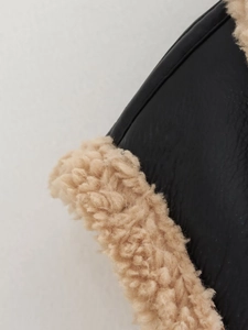 Détail rapproché du cuir noir mat et de la doublure en fausse fourrure beige d'un gilet