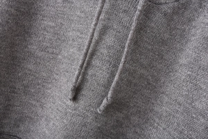 Detail of grey knitted sweater showing fine weave texture and matching drawstring hood cords