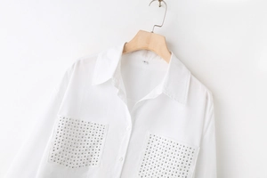 Detail of white cotton shirt with chest pockets decorated with silver metal studs