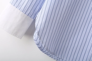 Détail d'une chemise à rayures bleues et blanches avec poignets blancs et ourlet arrondi