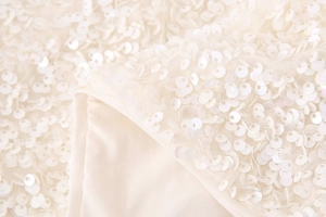 Close-up of white sequin fabric detail showing the sparkling texture and inner lining