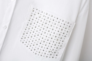 Detail of white poplin shirt featuring silver metal studs on front pocket and button