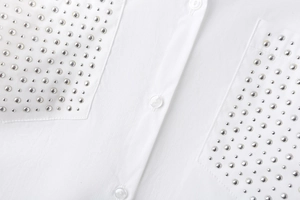 Detail of white cotton shirt featuring heavy duty silver dome studs on chest pockets