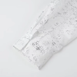 Detailed macro view of white shirt sleeve featuring silver foil printed pattern and button