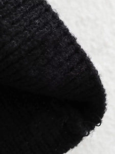 Macro detail of the black ribbed knit fabric showing the soft wool texture and fine stitching