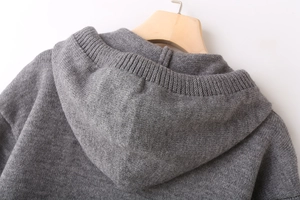 Detailed close-up of mid-gray knitted hoodie texture with ribbed hem on a wooden hanger