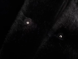 Detailed macro view of black faux fur jacket texture and silver metallic button fastener