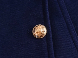 Macro shot of an embossed gold crest button on the navy blue twill fabric of the coat