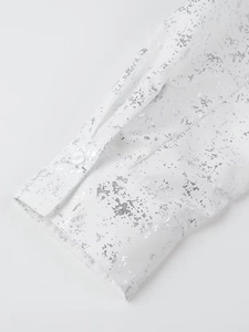 Close-up of white Y2K shirt cuff with metallic silver foil print and single button detail