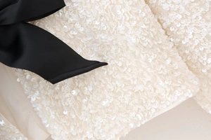 Détail de paillettes blanches avec un nœud en ruban noir sur un haut Y2K à manches longues