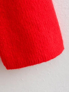 Macro shot of red rib-knit texture and soft fabric fibers on a slim sweater sleeve