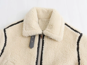 Détail macro d'une veste en peau lainée beige avec garnitures en cuir noir et zip en métal