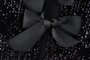 Détail du tissu à paillettes noires avec un grand nœud sur un haut Y2K cintré