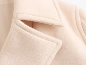 Detailed close-up of light beige wool coat collar with refined stitching and lapel texture
