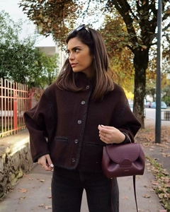 Detail of short brown wool jacket with contrast piping and textured burgundy leather handbag
