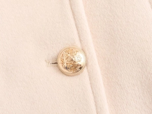 Close-up of golden lion crest button on premium beige wool coat with refined texture