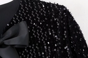 Détail d'un haut en velours noir avec paillettes brillantes et un grand nœud en gros-grain