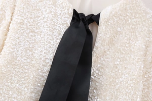 Detail of white sequined fabric featuring a black ribbed ribbon bow for a Y2K aesthetic