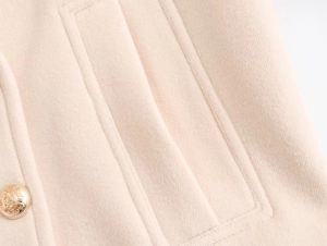 Close-up of beige wool coat featuring a gold embossed crest button and pocket stitching