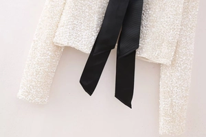 Detailed macro view of white sequin texture and black satin bow on Y2K slim blouse