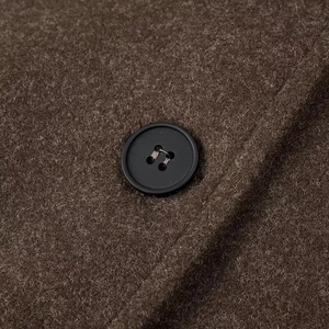 Macro shot of brown wool texture and a black four-hole button on the cropped jacket