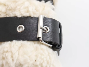 Détail de la boucle en cuir noir et œillets argentés sur la veste Y2K en faux mouton blanc