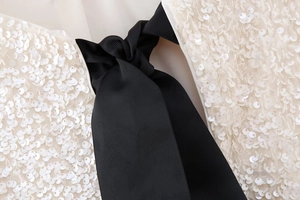 Detail of white sequins texture with a black ribbed ribbon bow on a slim fit top