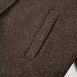 Detailed macro view of dark brown wool jacket showing a clean welt pocket and fabric texture