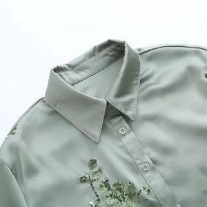 Detail of sage green satin shirt showing floral sequin embroidery and sleek buttons
