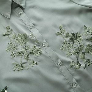 Close-up of sage green satin shirt showing intricate sequin floral embroidery details