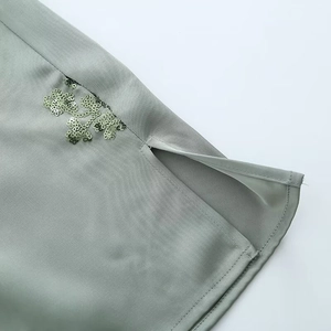 Close-up of green satin shirt hem with sequin embroidery and side slit detail