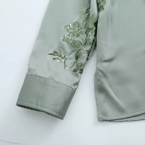 Detailed view of sequin floral embroidery on olive green satin long-sleeve shirt cuffs