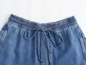 Detalle de vaqueros azules con cintura elástica, cordón con lazo y costuras de contraste