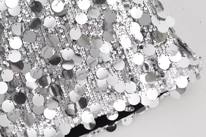 Détail de sequins argentés superposés sur le tissu d'une mini-jupe à taille haute
