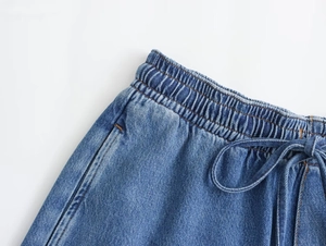 Detalle de cintura elástica con cordón y costuras naranjas en pantalón vaquero