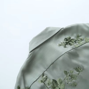 Macro detail of sage green satin shirt showing floral sequin embroidery on back shoulder
