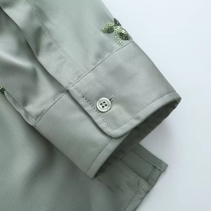 Detailed view of sage green satin cuff featuring intricate sequin embroidery and a button