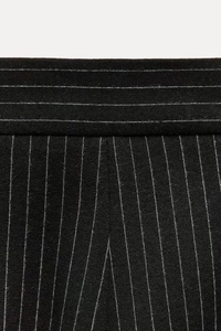 Detailed macro view of the pinstripe fabric and high waist stitching on black trousers