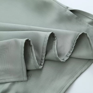 Close-up of sage green woven fabric showing fine stitching and a side slit detail