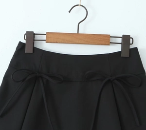 Detail of a black mini skirt featuring symmetric bow ties on a wooden hanger