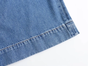Detalle de mezclilla azul lavado con pespuntes naranjas en el dobladillo del pantalón