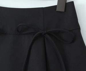 Detail of a black A-line mini skirt featuring a delicate ribbon bow on the waistline
