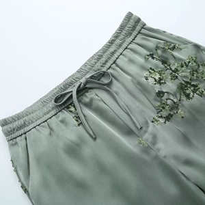 Detail view of sage green satin trousers with floral sequin embroidery and drawstring waist
