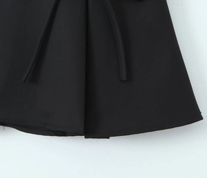 Close-up detail of black mini skirt featuring pleated fabric and matching decorative tie cord