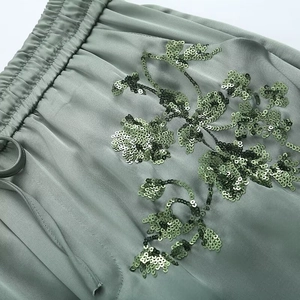 Detailed close-up of sage green satin trousers with sequin floral embroidery and drawstring