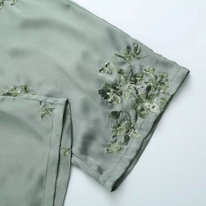 Detail showing sage green satin fabric with delicate sequin floral embroidery and silk finish