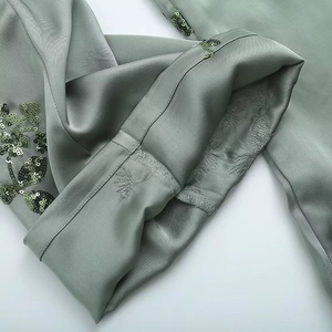 Detail of sage green fabric showing sequin floral embroidery and precise seam stitching