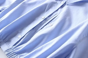 Detail view of light blue shirt with white buttons and elasticized gathered hem design