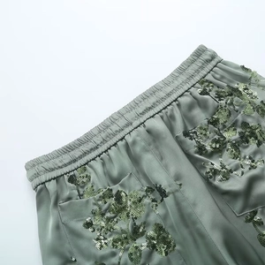 Detail of sage green satin pants featuring floral sequin embroidery and elastic waist